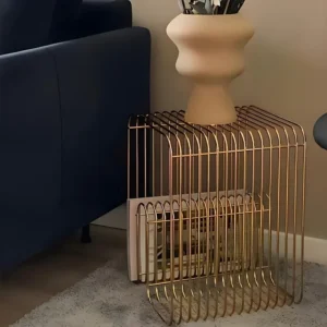 Brushed gold curved wire side table beside a navy sofa, with magazines stored in the frame