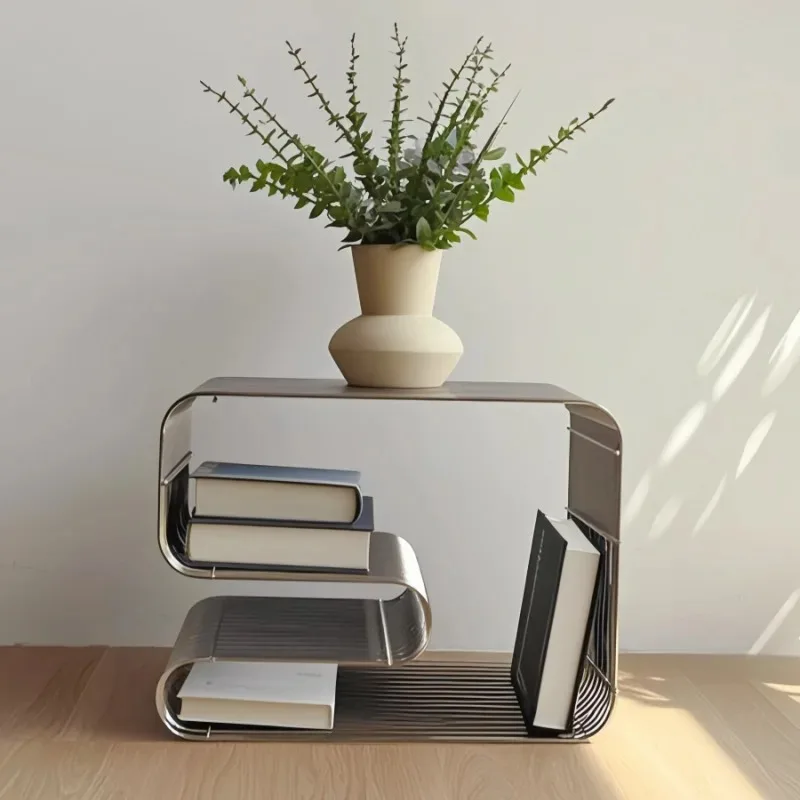 Brushed silver curved wire side table against a white wall with books slotted beneath the top